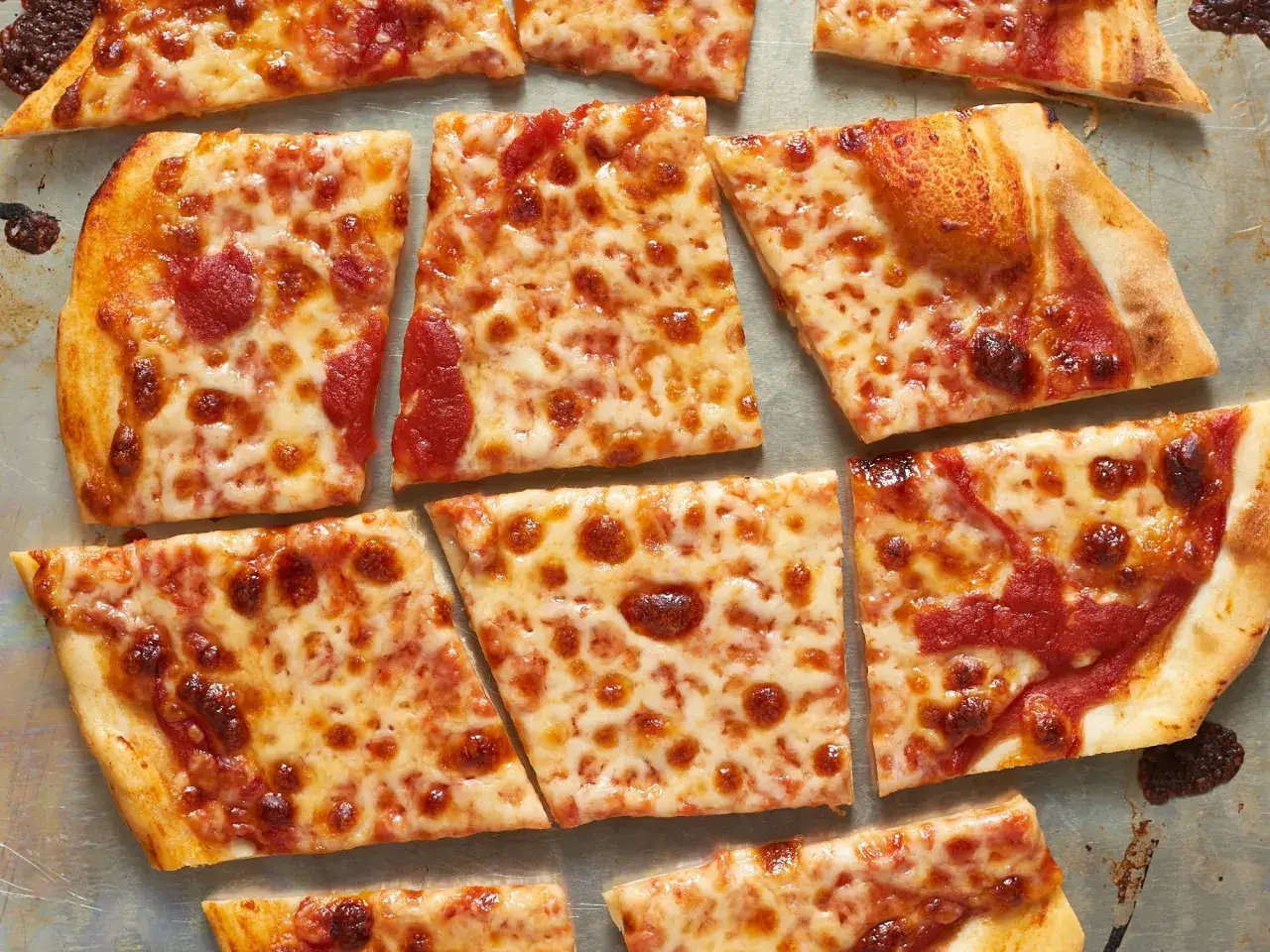 Kawałki pysznej pizzy na cienkim cieście, z ciągnącym się serem i sosem pomidorowym, ułożone na blasze.