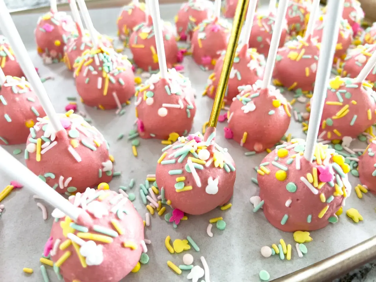Różowe cake pops z kolorową posypką i króliczkami, gotowe do świętowania.