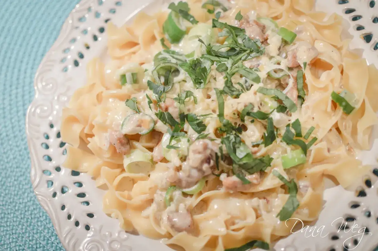 Makaron tagliatelle z kremowym sosem cebulowym, kawałkami boczku i zieloną cebulką, posypany świeżymi ziołami.