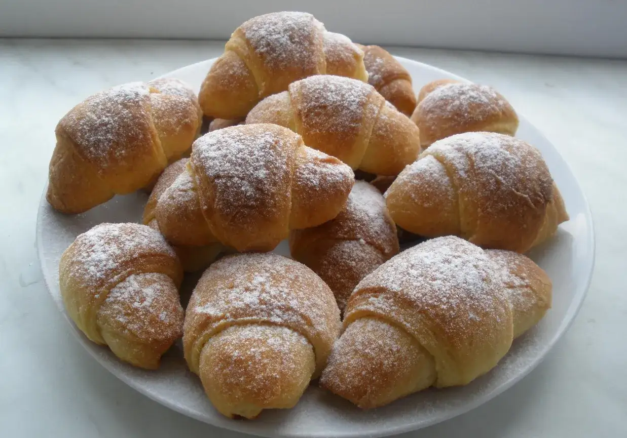 Stosik pysznych, domowych rogalików z marmoladą, posypanych cukrem pudrem. Idealne na deser.