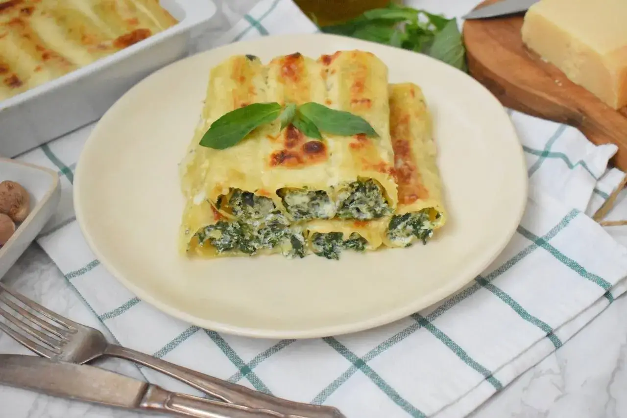 Pyszne cannelloni ze szpinakiem i serem, zapieczone pod beszamelem, ozdobione listkiem bazylii.