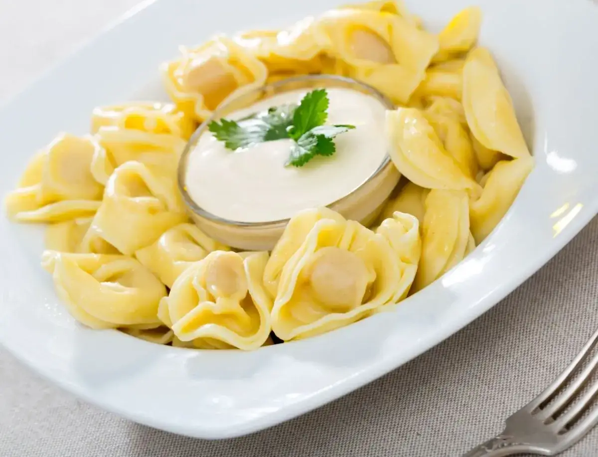 Pyszne pierożki tortellini z kremowym sosem śmietanowym, udekorowane natką pietruszki. Idealne na szybki obiad.