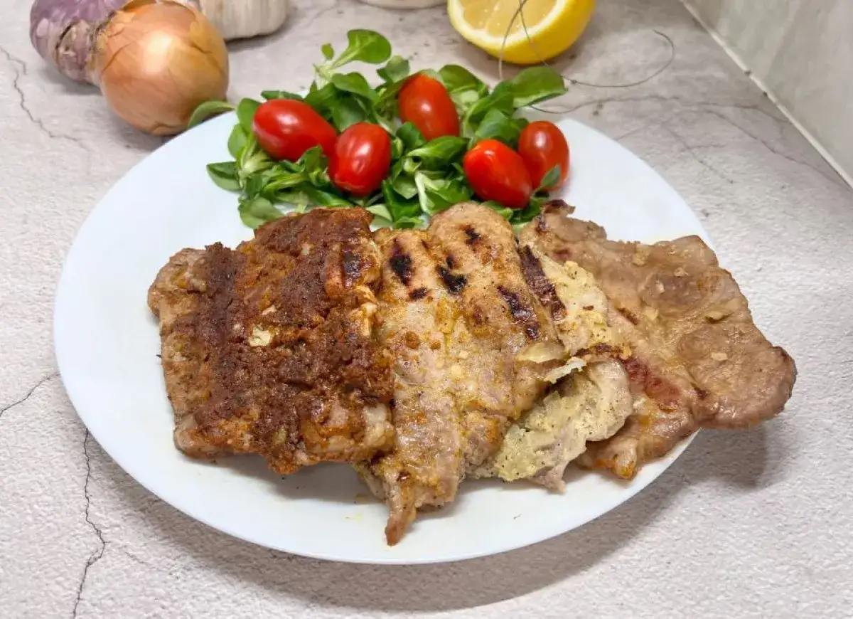 Karkówka z grilla, idealnie doprawiona marynatą, podana z sałatką i pomidorkami. Pyszne danie na letni obiad.