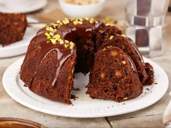 Pyszna babka na oleju, polana czekoladą i posypana pistacjami, z kawałkiem ciasta obok.