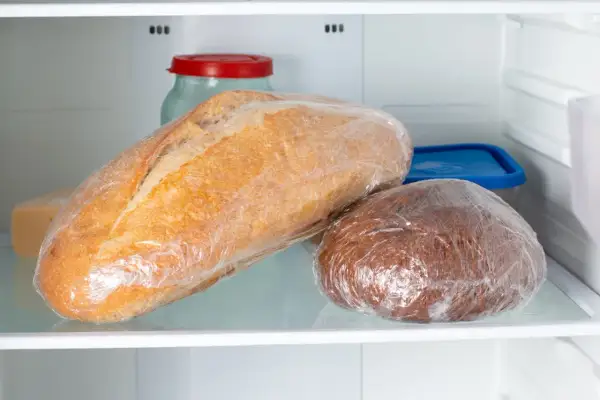 Dwa bochenki chleba, jeden jasny, drugi ciemny, zawinięte w folię spożywczą, leżą na półce lodówki. To może być odpowiedź na pytanie, dlaczego chleb pleśnieje.