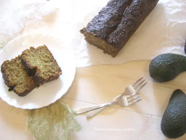 Chleb bananowy z awokado, pokrojony na kromki, leży na talerzu obok całego bochenka. Dwa awokado i widelce dopełniają kompozycję.
