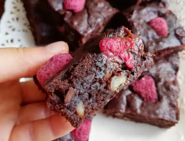 Pyszne brownie z malinami i orzechami, trzymane w dłoni.