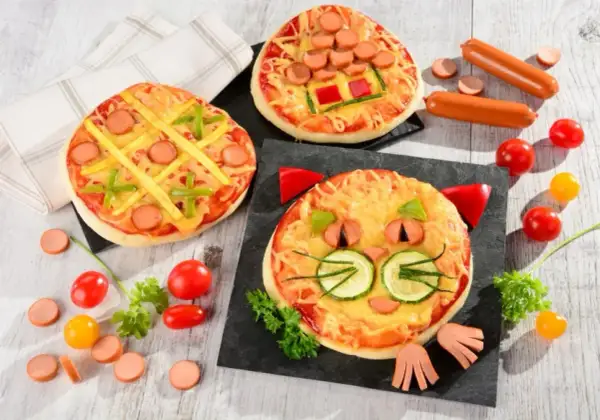 Wesołe pizza dla dzieci: jedna w kształcie kota, druga jak kółko i krzyżyk, trzecia z parówkami i papryką.
