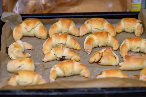 Szybkie rogaliki kruche, lekko zarumienione, ułożone na blasze wyłożonej papierem do pieczenia. Niektóre z nadzieniem.