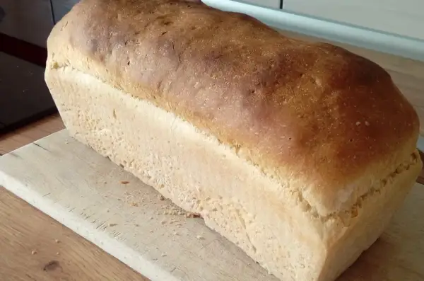 Puszysty chleb na suchych drożdżach, z chrupiącą skórką, leży na drewnianej desce. Idealny do kanapek.