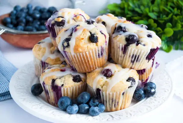 Stos pysznych muffinek z borówkami, polanych lukrem, ozdobionych świeżymi borówkami. Idealne na śniadanie lub deser.