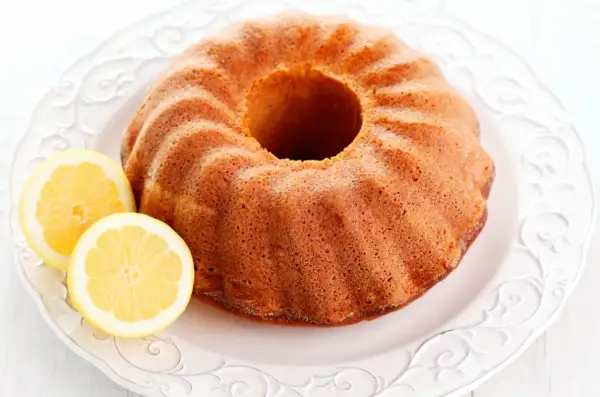 Puszysta babka cytrynowa na ozdobnym talerzu, z dwoma plasterkami cytryny obok. Idealna na popołudniową herbatkę.