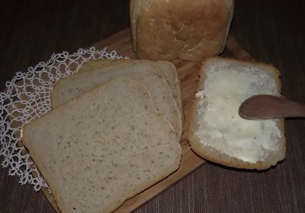 Chleb na zakwasie z maszyny, pokrojony w kromki, jedna posmarowana masłem.
