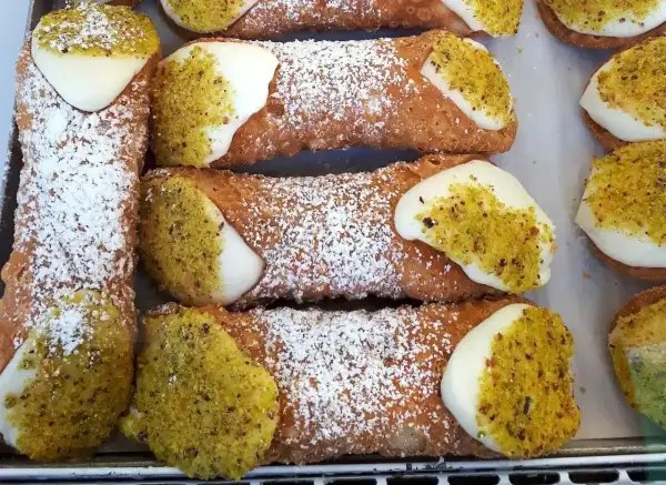 Chrupiące rurki z kremem, posypane cukrem pudrem i pistacjami, kuszą swoim wyglądem.