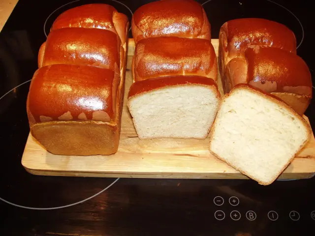 A fresh batch of chleb hokkaido, golden brown and fluffy, awaits. Two loaves are sliced, revealing their soft, airy crumb.