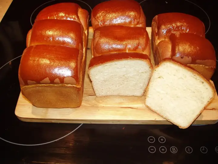 A fresh batch of chleb hokkaido, golden brown and fluffy, awaits. Two loaves are sliced, revealing their soft, airy crumb.